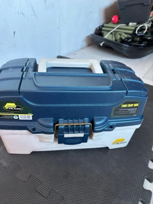 Säljer inte det som är i den - Säljer en blå och vit Plano fiskelåda med två utdragbara fack fyllda med olika fiskedrag och beten i flera färger. Lådan har ett rejält handtag och säker låsmekanism, perfekt för att organisera fiskeutrustning.