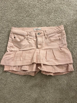 Rosa volangkjol från Esprit - Snygg ljusrosa kjol från Esprit med volangdetaljer nedtill. Klassisk femficksmodell med knapp och dragkedja framtill. Perfekta för en trendig och lekfull look under varma dagar.