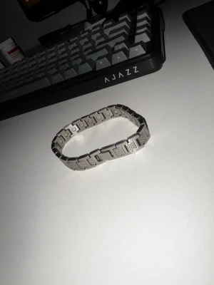 Stilrent armband i rostfritt stål - Säljer ett snyggt armband i silverfärgat rostfritt stål. Armbandet har en länkdesign med rektangulära sektioner och detaljerade mönster på varje länk. Perfekt accessoar för dig som gillar en clean och modern look.