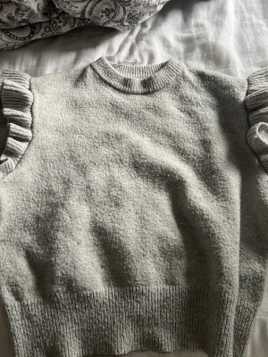 Grå stickad tröja med volangdetaljer - Säljer denna stickad tröja med volang på axlarna ftån gina young. Den har använts så är lite noppring därav priset men inga andra tecken på användning, bara och höra av sog vid frågor eller funderingar💞💞