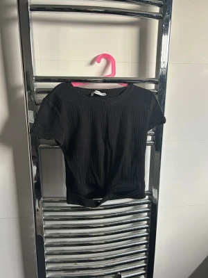 Svart ribbad croppad topp - En svart croppad topp med ribbad struktur och korta ärmar. Toppen har en enkel rund halsringning och är gjord i ett mjukt material som passar perfekt till jeans eller kjol. Snygg och enkel att matcha med olika outfits.