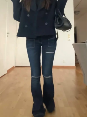 Mörkblå bootcut jeans med slitningar - Snygga mörkblå bootcut jeans med slitningar vid knäna och detaljerade sömmar. Jeansen har en klassisk femficksmodell och lätt utsvängda ben. Perfekta för en trendig och avslappnad look.