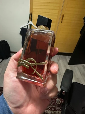 Yves Saint Laurent Libre Le Parfum  - Säljer en snygg parfym från Yves Saint Laurent, Libre Eau de Parfum. Flaskan är rektangulär i genomskinligt glas med guldig YSL-logga och svart asymmetrisk kork. Innehållet är bärnstensfärgat och flaskan har lyxiga detaljer i metall. Använt bara två gånger! OBS! Saknar original förpackning!
