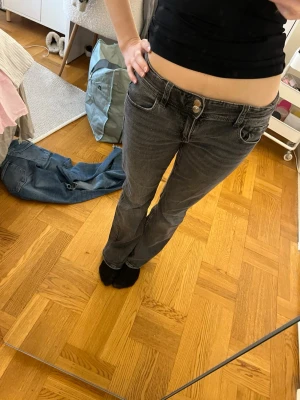 Gråa low waist och bootcut jeans - Säljer ett par gråa jeans med låg midja och som är bootcut. Superfina fickor där bar med vitt mönster.