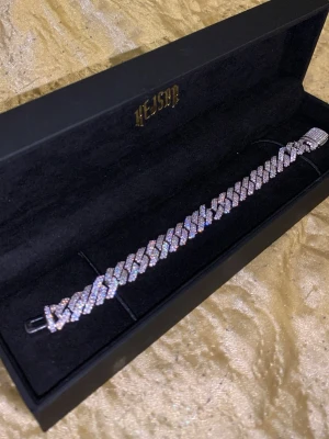 Iced ut kedjearmband från kejsar - Säljer ett glittrande iced ut kedjearmband från kejsar. Armbandet är silverfärgat och täckt med små gnistrande stenar som ger en lyxig känsla. Kommer i original svart ask med guldfärgad logga. Perfekt för dig som gillar statement-smycken. Helt ny använd 2gånger