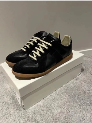 Svarta sneakers med mockadetaljer - Snygga svarta sneakers med ovandel i läder och mocka, vita snören och klassisk gummisula i brunt. Skorna har en stilren och tidlös design som passar till många olika outfits. Perfekt för dig som gillar minimalistisk och clean stil.