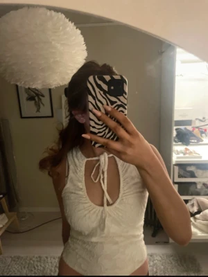 Vit ärmlös topp med knyt och struktur - Säljer en vit ärmlös topp med snygg struktur och knyt fram vid halsen. Toppen har en rundad urringning med öppning och är figurnära i modellen. Perfekt för dig som gillar trendiga och stilrena plagg. Jätte gullig knappt använd