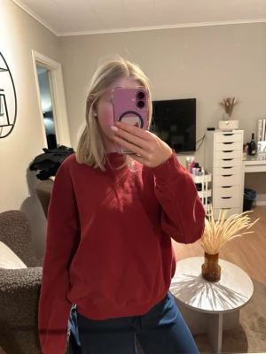 Röd sweatshirt från 157 - Röd sweatshirt från 157 med klassisk rund hals och ribbade muddar. Tröjan är enkel och stilren, perfekt för en avslappnad look. Materialet är mjukt och bekvämt, och passar bra till jeans eller joggers.