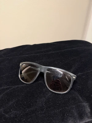 Svarta Ray-Ban Wayfarer solglasögon - Klassiska svarta Wayfarer solglasögon från Ray-Ban med mörka glas och ikonisk form. Snygg och tidlös design som passar till de flesta outfits. Tillverkade i plast med Ray-Ban-logga på linsen och metallnitar vid bågarna.