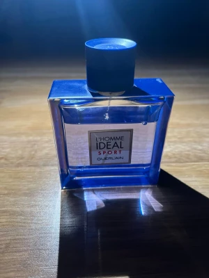 L'Homme Ideal Sport från Guerlain - L'Homme Ideal Sport från Guerlain är en parfym i en stilren, rektangulär glasflaska med intensivt blå färg och matchande blå kork. Flaskan har en modern design med tydlig etikett framtill. Perfekt för dig som gillar fräscha och sportiga dofter.