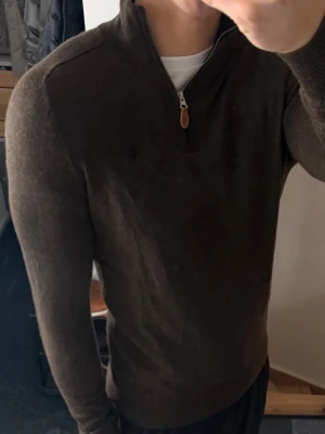 Morris half zip - Snygg mörkbrun stickad tröja från Morris med halv dragkedja och hög krage. Tröjan har långa ärmar, ribbade muddar och en diskret broderad logga på bröstet. Perfekt för en stilren och avslappnad look. Lappen är lite av men syns inte när man har den på. Storlek s men är liten i storleken så sitter som xs 