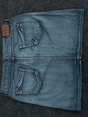 Blå jeanskjol med fickor - Snygg blå jeanskjol från L.O.G.G. med klassiska stora fickor både fram och bak. Kjolen har en rak passform och är tillverkad i slitstarkt bomullsdenim. Perfekt för dig som gillar en avslappnad och cool stil.