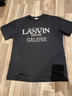 Svart Lanvin Galerie t-shirt - Cool svart t-shirt från Lanvin Galerie med tryck i vitt och grått på framsidan och ett stilrent logotryck på ryggen. Klassisk passform och korta ärmar, perfekt för dig som gillar streetstyle och snygga loggor. Materialet är mjuk bomull.