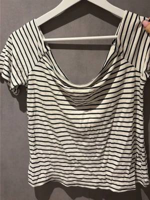 Randig offshoulder topp - Säljer en vit offshoulder topp med svarta tunna ränder. Toppen har korta ärmar och en lös, något croppad passform. Perfekt för dig som gillar en avslappnad och trendig stil. Skriv för fler frågor.❤️