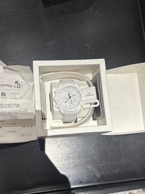  Omega x Swatch Speedmaster - Snygg vit Omega x Swatch Speedmaster med klassisk rund urtavla och vita detaljer. Klockan har ett sportigt och stilrent utseende med vit rem och tydliga markeringar på urtavlan. Perfekt för dig som gillar ikoniska samarbeten och modern design.