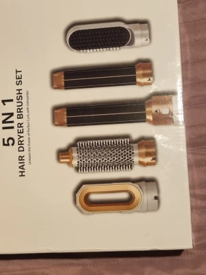 5-i-1 hårfön och stylingborste - Multifunktionell 5-i-1 hårfön och stylingborste med utbytbara tillbehör i svart, vitt och guld. Setet innehåller olika borstar och locktillbehör för att torka, borsta och styla håret. Perfekt för att skapa volym, lockar och släta frisyrer. Har ej använt och behöver ej längre 