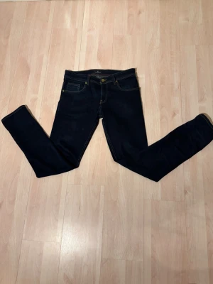 Louis Vuitton jeans - Snygga mörkblå slim fit jeans från Louis Vuitton med klassisk femficksdesign och kontrastsömmar. Jeansen har en stilren look med gulddetaljer vid knappar och nitar samt läderpatch bak i midjan. Perfekta för en trendig och avslappnad stil. W30 L32 men passar mer som W30/L32