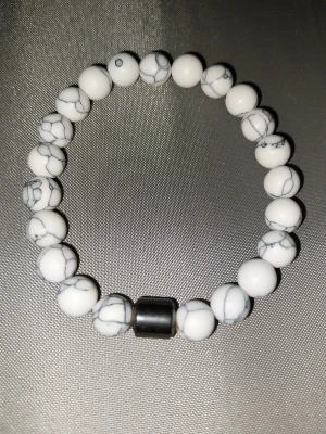 Grisch armband - Snyggt armband med vita pärlor som har grått marmormönster och en större svart pärla som accent. Perfekt för dig som gillar stilrena accessoarer med lite edge. Elastiskt band gör det enkelt att ta på och av. Passar till många olika outfits.