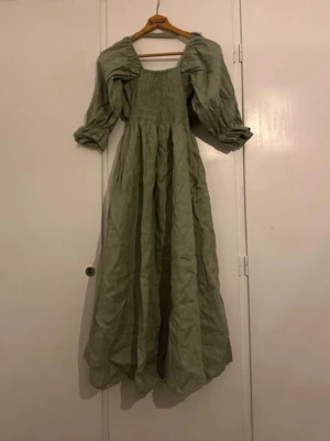 Grön långklänning med puffärmar - Ljusgrön långklänning med puffiga trekvartsärmar och markerad midja. Klänningen har en omlott-detalj i ryggen och är tillverkad i ett luftigt linnematerial. Nypris 3000 kr.