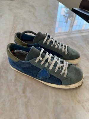 Blå och gröna sneakers från Philippe Model - Snygga sneakers från Philippe Model i blått och grönt mocka och textil. Skorna har vita snören, blå detalj på sidan och beige sula. Men ser har en defekt på tån på ena skon men de lite sko lim så är de som nya 👟🔥box ingår tyvärr inte där av ett lägre pris