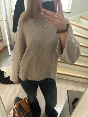 Beige stickad tröja med vida ärmar - Mysig beige stickad tröja med rund hals och vida ärmar. Tröjan har en avslappnad passform och ribbade muddar vid ärmslut och nederkant. Perfekt för lager på lager och enkel att matcha med jeans eller kjol.