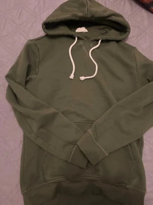 Pier one hoodie med vit dragsko - En stilren olivgrön hoodie med klassisk huva och vita dragsnören. Hoodien har en känguruficka framtill och är tillverkad i mjukt material som känns skönt mot huden. Perfekt för en avslappnad look.