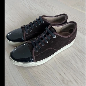 Lanvin - Snygga sneakers i vinröd mocka med svarta skosnören och lackad svart tå. Skorna har vita sulor och detaljer i mörkbrunt läder runt kanterna. Perfekta för dig som gillar en stilren och unik look.
