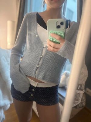 Ljusblå stickad kofta från ONLY - Söt ljusblå stickad kofta från ONLY med v-ringning och dekorativa pärlknappar framtill. Koftan har lång ärm och ribbade muddar vid ärmslut och nederkant. Perfekt att slänga över ett linne för en chill look.