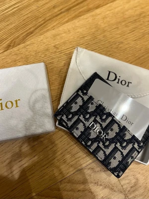 CD cardholder - cd cardholder. Tillverkad i canvas och läder med flera fack för kort. Perfekt accessoar för dig som vill ha något stilrent och lyxigt i fickan. Kommer med original ask och dustbag