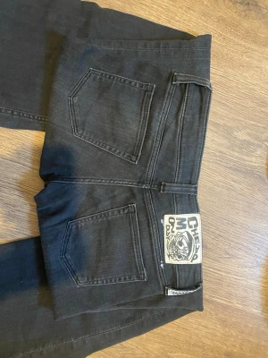 Svarta Cheap Monday jeans bootcut - Säljer ett par svarta jeans från Cheap Monday med bootcut-modell. Köpa secondhand men passade tyvärr inte. Jeansen har klassiska fem fickor, svart tvätt och en stor logopatch bak. Materialet är denim med en stretch för skön passform. Perfekta för dig som gillar en avslappnad men trendig look.💞🤗