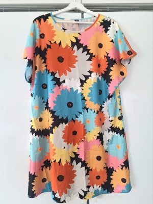 Färgglad blommig klänning Shein Curve - Kortklänning från Shein Curve med stort blommigt mönster i orange, blått, gult, rosa, vitt och svart. Klänningen har rund halsringning och korta ärmar. Perfekt för dig som gillar färg och vill sticka ut med en lekfull stil.