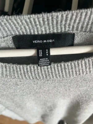 Grå stickad tröja från Vero Moda - Snygg grå stickad tröja från Vero Moda med rund halsringning och ribbade muddar. Tröjan har en enkel och clean design som passar perfekt till jeans eller kjol. Tillverkad i mjukt material för en bekväm känsla.