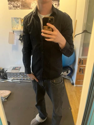 Svart skjorta från Selected Homme - Säljer en stilren svart skjorta från Selected Homme. Skjortan har klassisk krage, långa ärmar och knappar framtill. Tillverkad i mjuk bomull och har en slim passform som sitter snyggt på kroppen. Perfekt för dig som gillar en clean och enkel look.