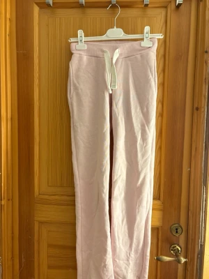 Ljusrosa mjukisbyxor Gina Tricot - Säljer ett par ljusrosa mjukisbyxor från Gina Tricot med dragsko i midjan och ribbad kant upptill. Byxorna har raka ben och är gjorda i ett mjukt, fleeceliknande material som är perfekt för chill dagar. Supersnygga och bekväma att ha på sig!
