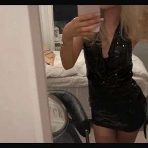 Svart glittrig kort klänning - Snygg svart kort klänning med glittriga paljetter och djup v-ringning. Klänningen är ärmlös och har en figurnära passform som framhäver siluetten. Perfekt för dig som vill sticka ut och glänsa.