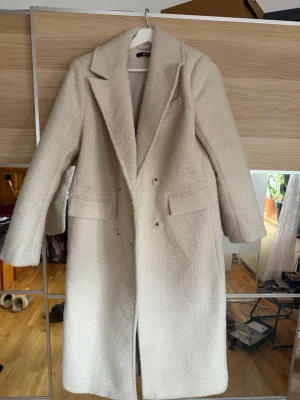 Ljusbeige teddy-kappa Gina Tricot - Säljer en lång, ljusbeige teddy-kappa från Gina Tricot. Kappan har dubbelknäppning, breda slag och två fickor framtill. Materialet är fluffigt och ger en trendig look. Perfekt för dig som vill ha en stilren och mysig kappa till hösten och vintern.