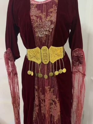 Vinröd långklänning med guldbälte - Elegant vinröd långklänning i sammet med broderade blommor och detaljer i guld. Klänningen har långa ärmar i transparent tyg och ett brett guldfärgat bälte med hängande mynt. Perfekt för dig som vill sticka ut med en unik look. Obs bältet kommer inte med