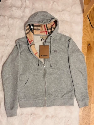 Burberry zip - grå - With tag. Gray burberry zip hoodie with name on zipper and laces✅ Length 60 cm✅ Width - waist: 45cm,✅  chest: 50cm✅ Very warm and comfortable🔥 100% cotton💯         Fråga om du har frågor,