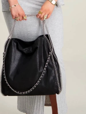 Svart handväska med kedjedetaljer - Stilren svart handväska i mjukt material med silverfärgade ked CCedjor längs kanterna och som axelrem. storyn är rymlig och har en avslapp lambad form, perfekt för dig som gillar trendiga accessoarer med attityd. Pass backbone till dig4 som vill sticka sop ut.