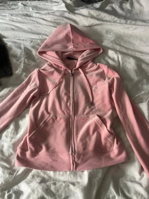 Juicy Couture hoodie  - Säljer en ljusrosa juicy couture hoodie med dragkedja och huva. Hoodien har två stora fickor framtill och justerbara snören i huvan. Materialet känns mjukt och skönt, perfekt för chill dagar. Liten broderad logga på bröstet för en clean look.