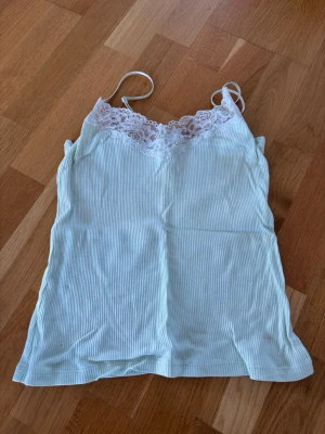 Vit ribbad linnetopp med spets - Söt vit ribbad linnetopp med tunna axelband och spetsdetaljer upptill. 