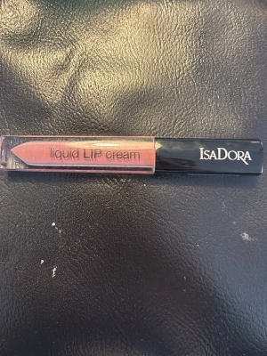 IsaDora Liquid Lip Cream nude rosa - IsaDora Liquid Lip Cream i en snygg nude rosa nyans. Kommer i en smidig tub med svart lock och applikator för enkel applicering. Ger en krämig finish och känns mjuk på läpparna. Perfekt för dig som gillar naturliga toner och glossig look.