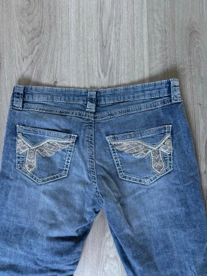 Blå bootcut jeans  - Säljer ett par blå bootcut jeans från Gina Tricot med slitningar på benen och snyggt broderade bakfickor. Passar bra i längden på mig som är drygt 170 cm. Knappt använda. Midjemått: 74 cm Innerbenslängd: 79 cm