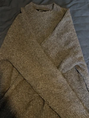 Gråmelerad stickad tröja - Mysig gråmelerad stickad tröja med avslappnad passform. Tröjan har långa ärmar och är tillverkad i ett mjuktultigt material som passar perfekt för kyligare dagar.