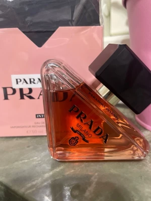 Prada Paradoxe Intense parfym 50ml - Prada Paradoxe Intense är en exklusiv parfym i en soppsnygg, trekantig glasflaska med svart fyrkantigt lock. Flaskan har en rosa-orange tonad vätska och elegant svart text. Kommer i en rosa kartong med svart och vit detalj. Doften är modern och lyxig.