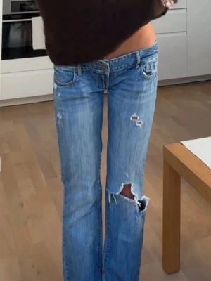 Blå slitna jeans Abercrombie & Fitch - Säljer ett par clusterblå jeans från Abercrombie & Fitch med slitningar och hål emellan benen och på låret. Jeansen har klassisk femficks confront och låg midja. 