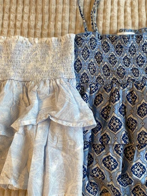 Två blåmönstrade tubtoppar Gina Tricot - Säljer två snygga tubtoppar från Gina Tricot i storlek 134/140. Ena toppen är ljusblå med paisleymönster och volangdetalj, den andra är mörkare blå med grafiskt mönster. Båda är smockade upptill och perfekta för sommaren. Har tyvärr tappat bort banden till den ena men minst lika snygg utan! Säljer båda för sig eller tillsammans. Pris kan diskuteras, cirka 300 för båda💞