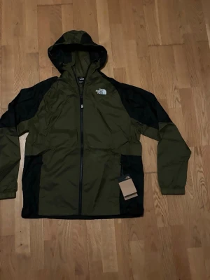 Windbreaker The North Face -  The Northface windbreaker I olive grön och svart fargkombination, helt ny och oanvant. Jackan är i storlek M. Jackan är dessutom packbar 