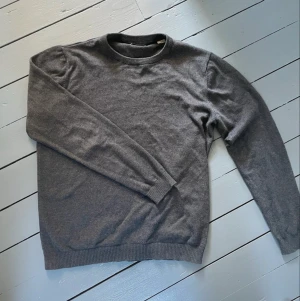 Mörkgrå stickad tröja - En enkel och stilren mörkgrå stickad tröja med rund halsringning och långa ärmar. Tröjan har ribbade muddar vid ärmslut och nederkant. Perfekt basplagg för lager på lager och passar till det mesta.