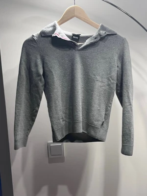 Grå slim fit tröja från Hugo Boss - Snygg grå tröja från Hugo Boss i slim fit-modell, tillverkad av finaste italienska garn. Tröjan har lång ärm, klassisk krage och diskreta ribbade muddar. Perfekt för dig som gillar stilrena och exklusiva plagg.